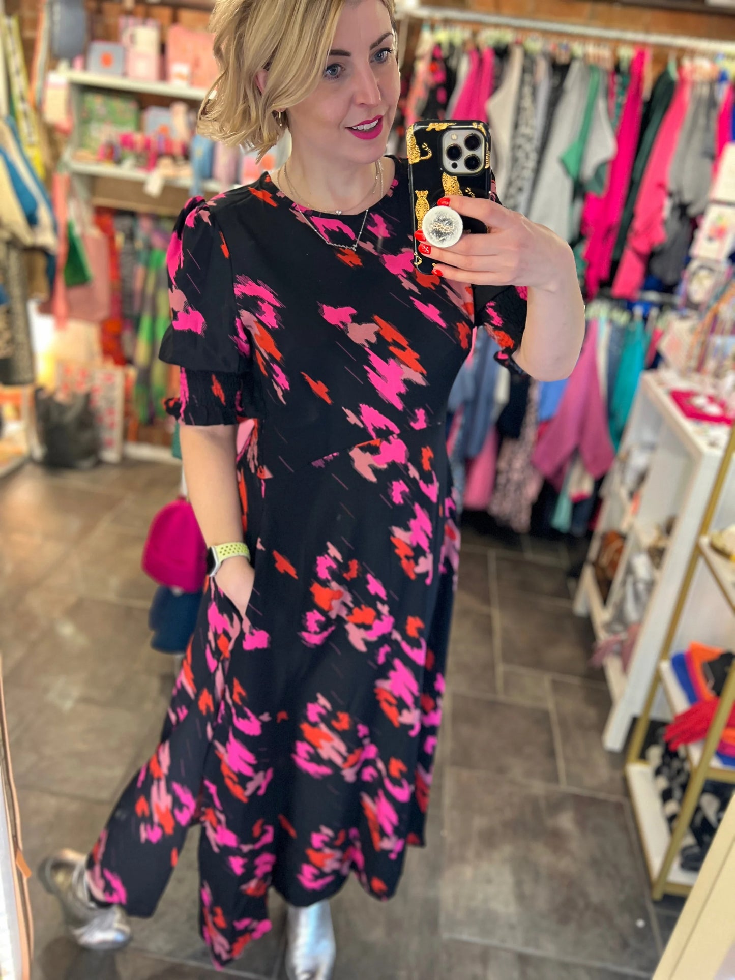 Woman taking a mirror selfie wearing a black dress with colorful patterns in a store.