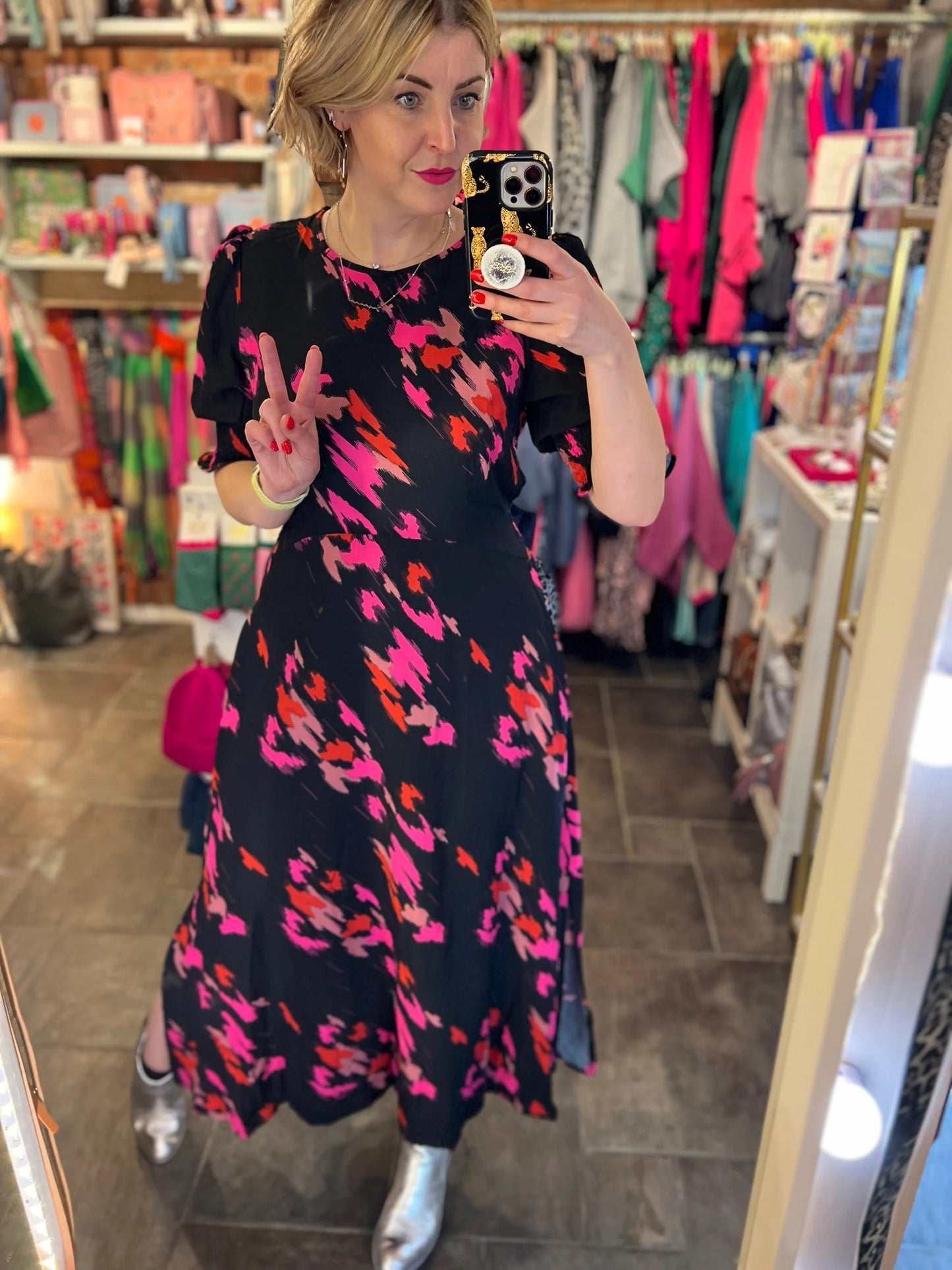 Woman taking a mirror selfie wearing a colorful dress in a store.
