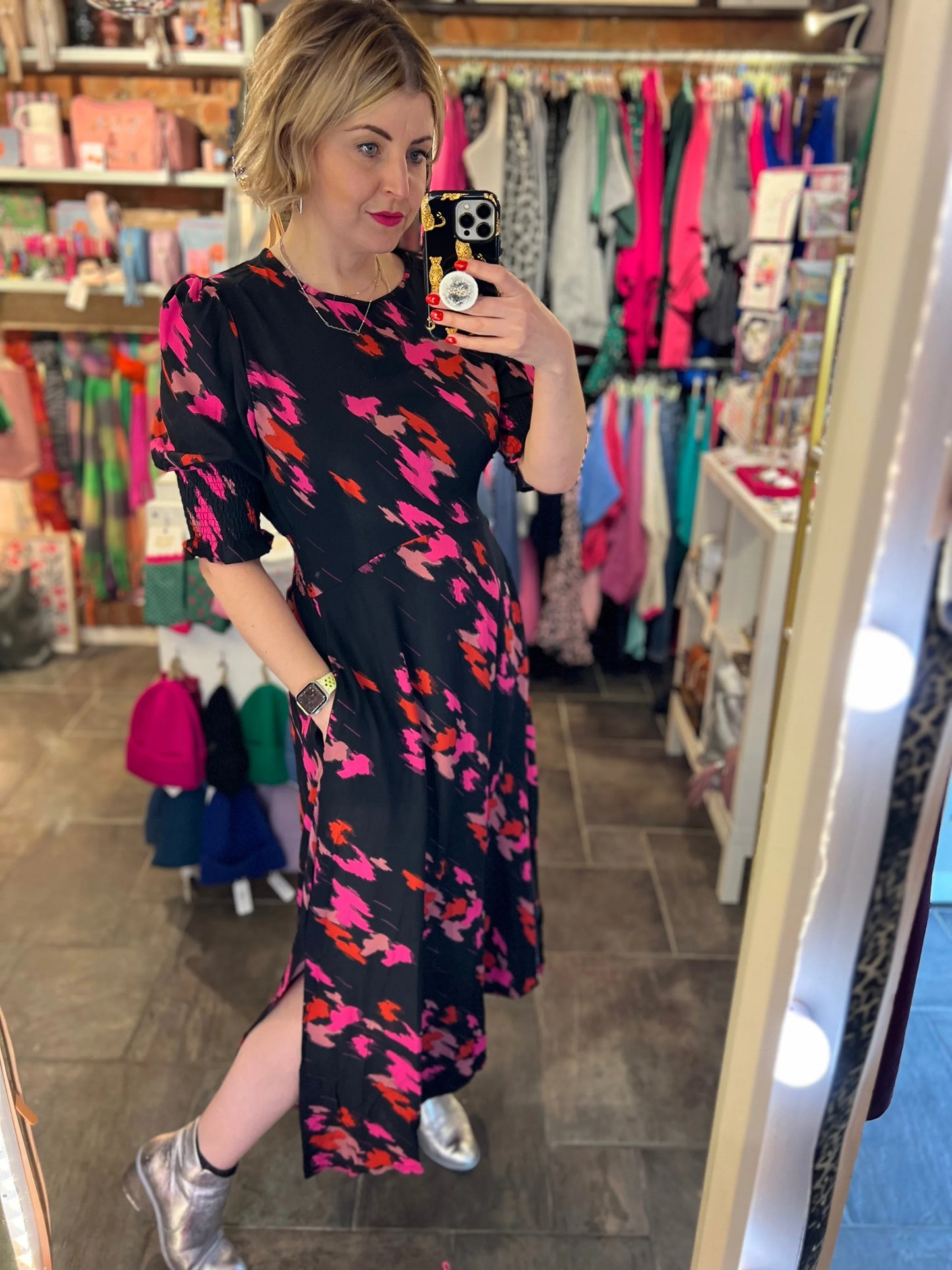 Woman taking a mirror selfie wearing a floral dress in a clothing store.