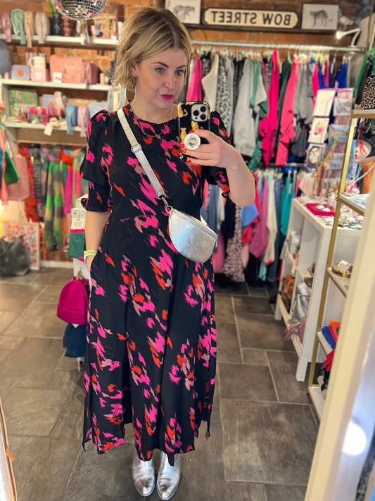Woman taking a mirror selfie wearing a colorful dress in a store.