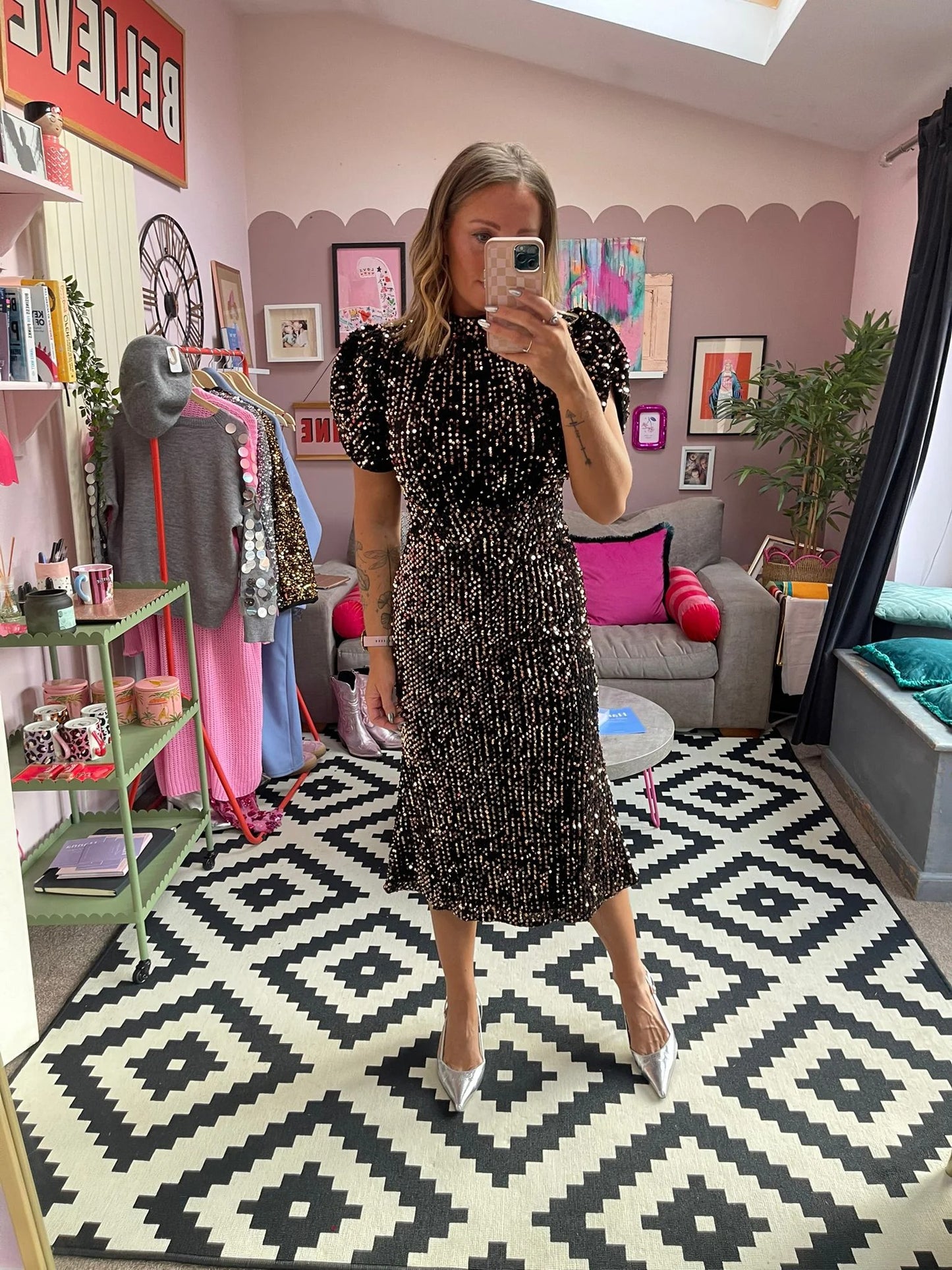 Woman taking a mirror selfie in a room with a patterned rug, colorful pillows, and decor.
