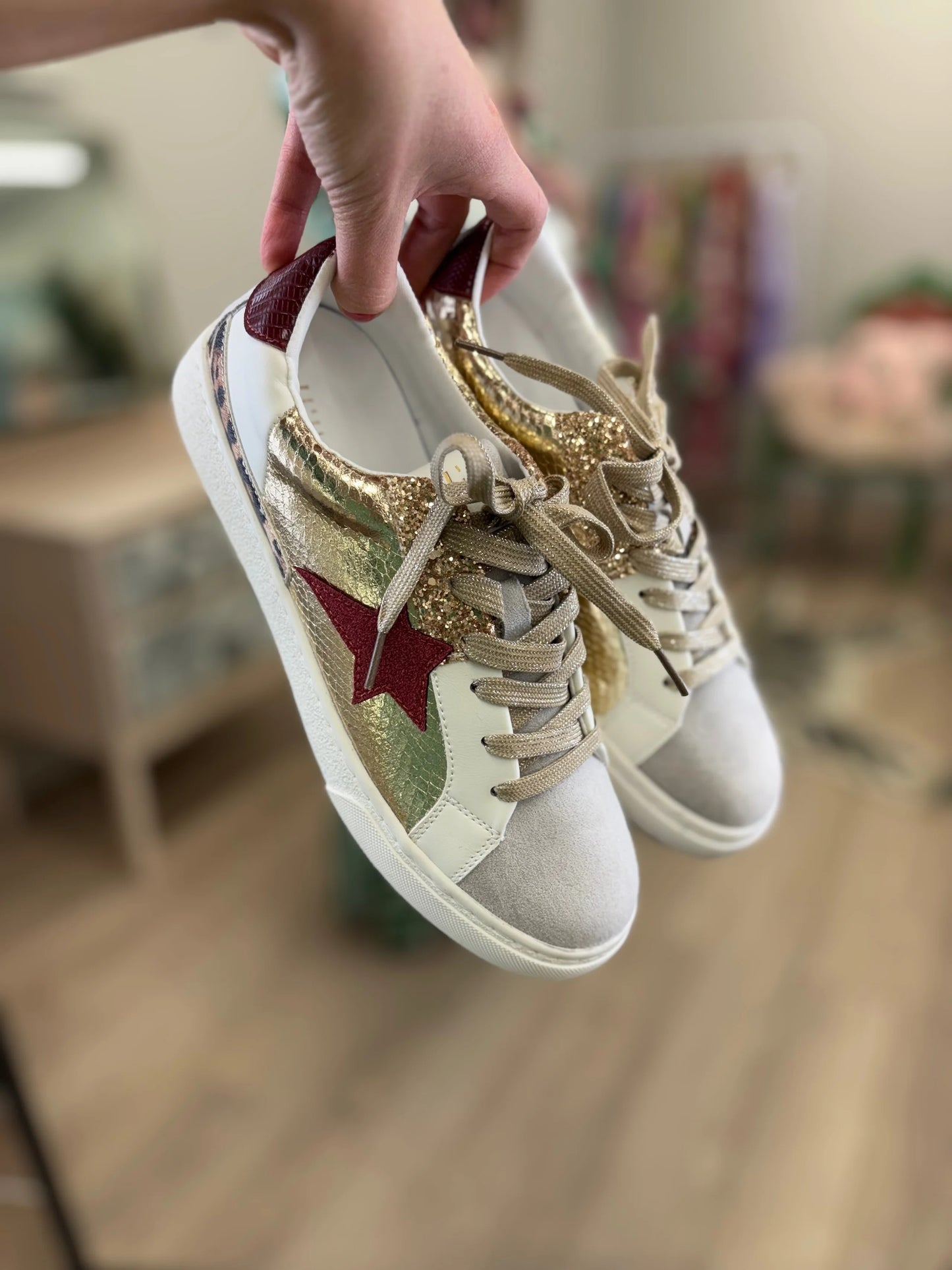 Beige sneakers with a red star held by a hand in an indoor setting