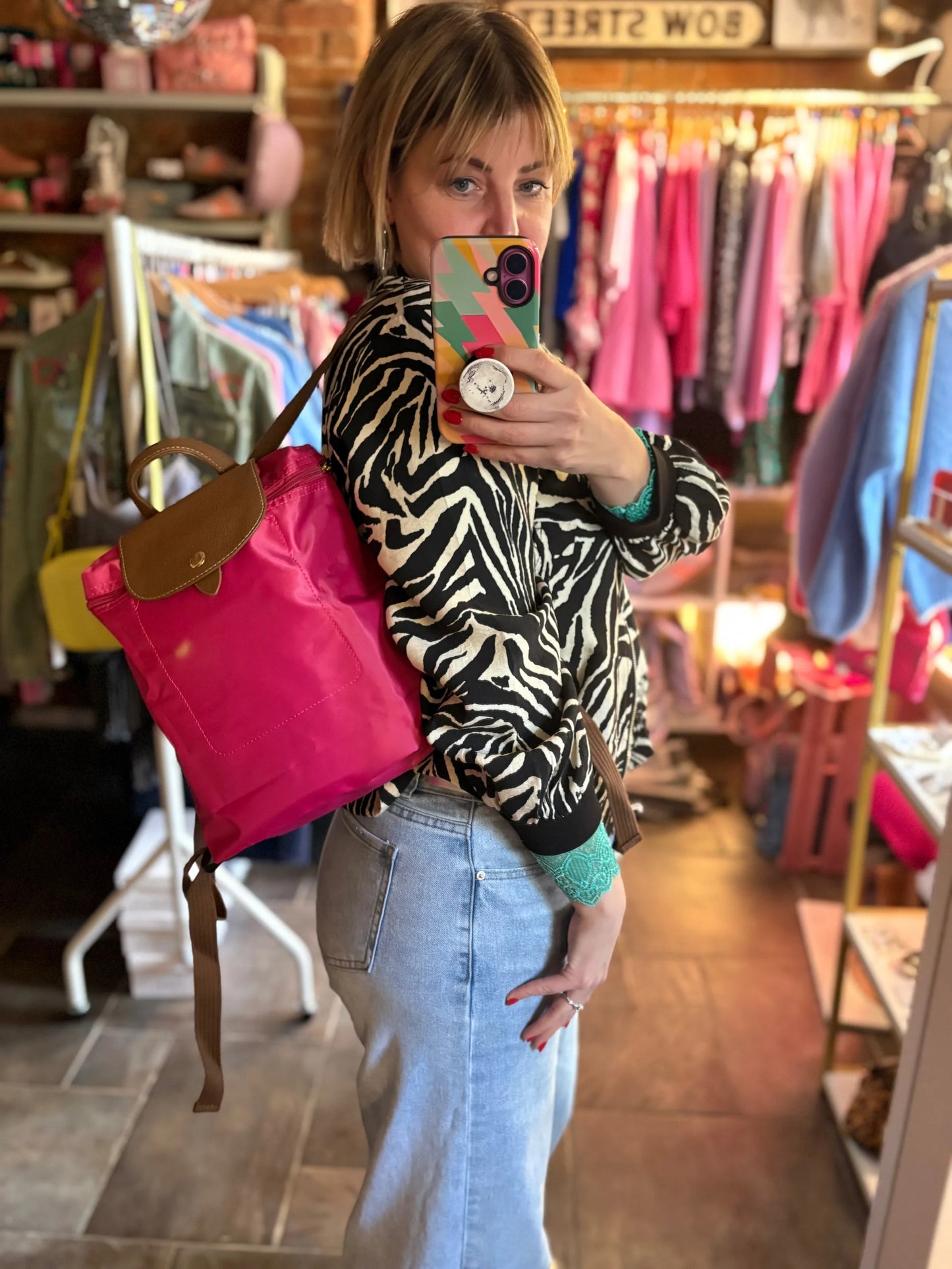 Person taking a mirror selfie in a store with a zebra print jacket and pink backpack.