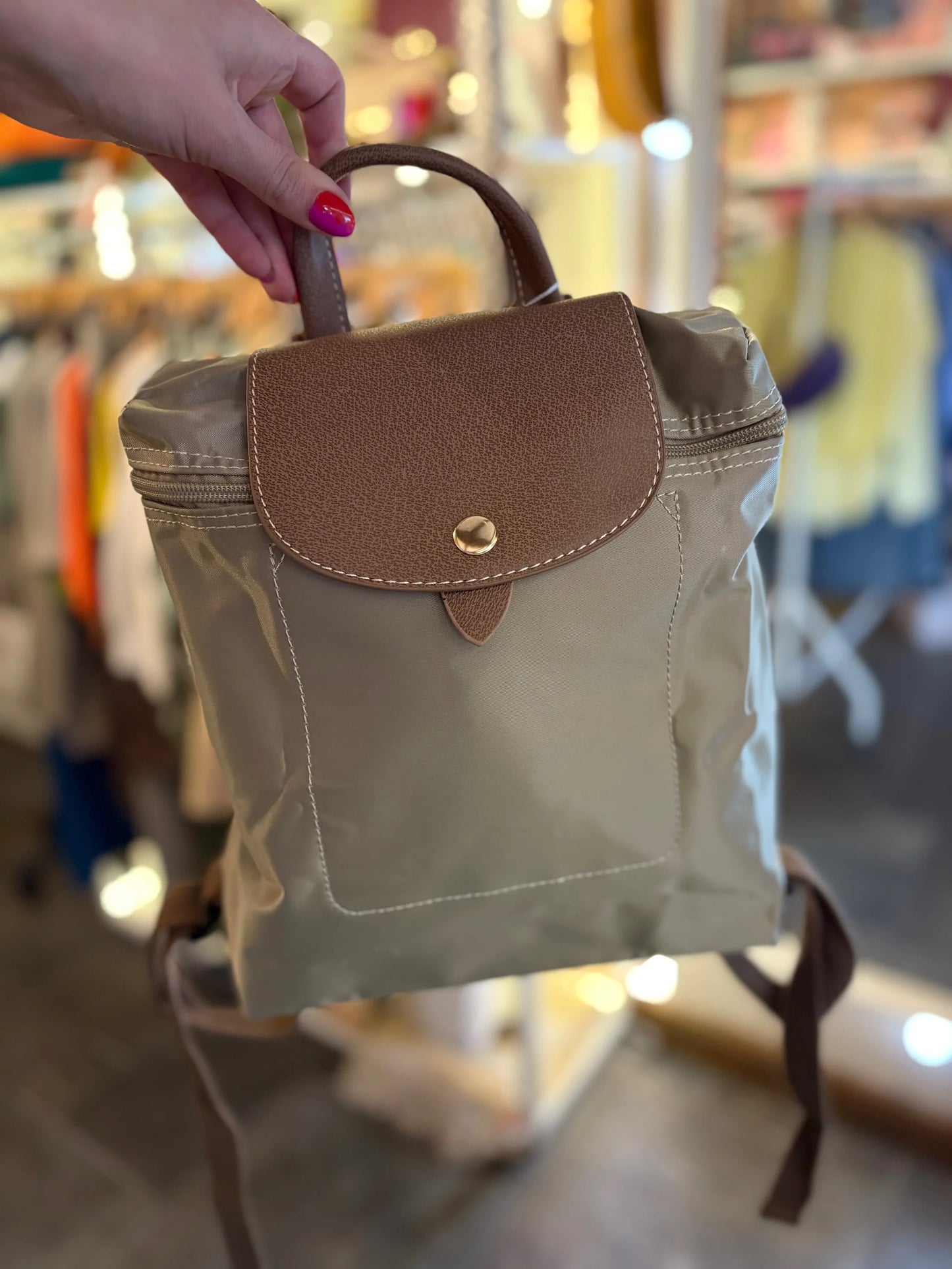 Hand holding a small brown and beige backpack in a store setting