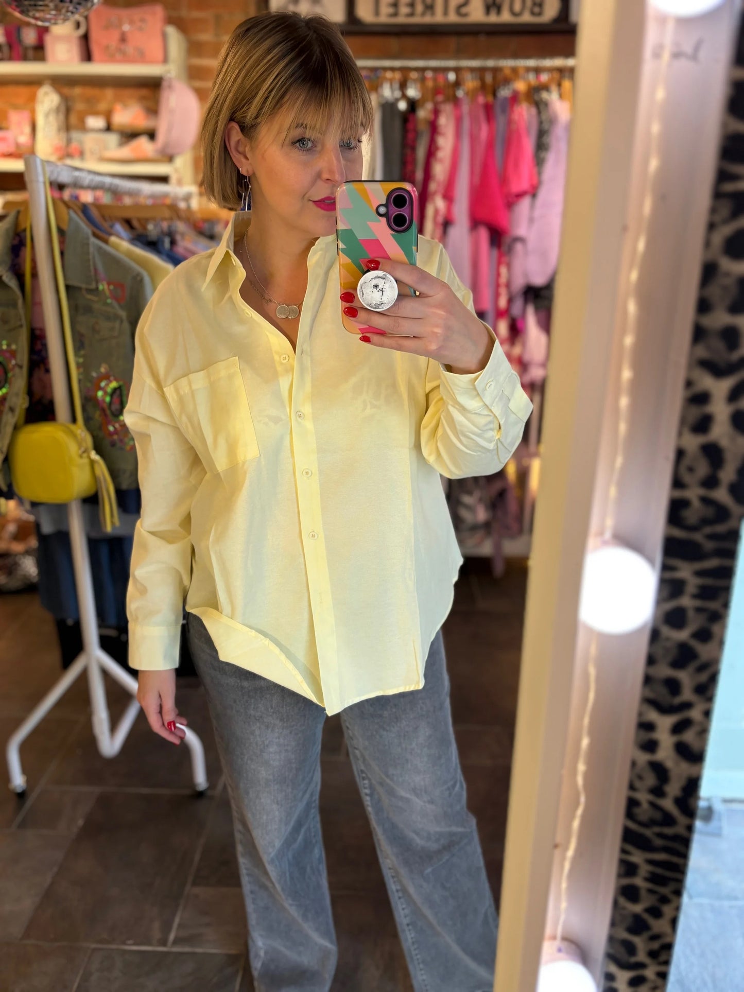 Woman taking a mirror selfie wearing a light yellow shirt and blue jeans in a store.