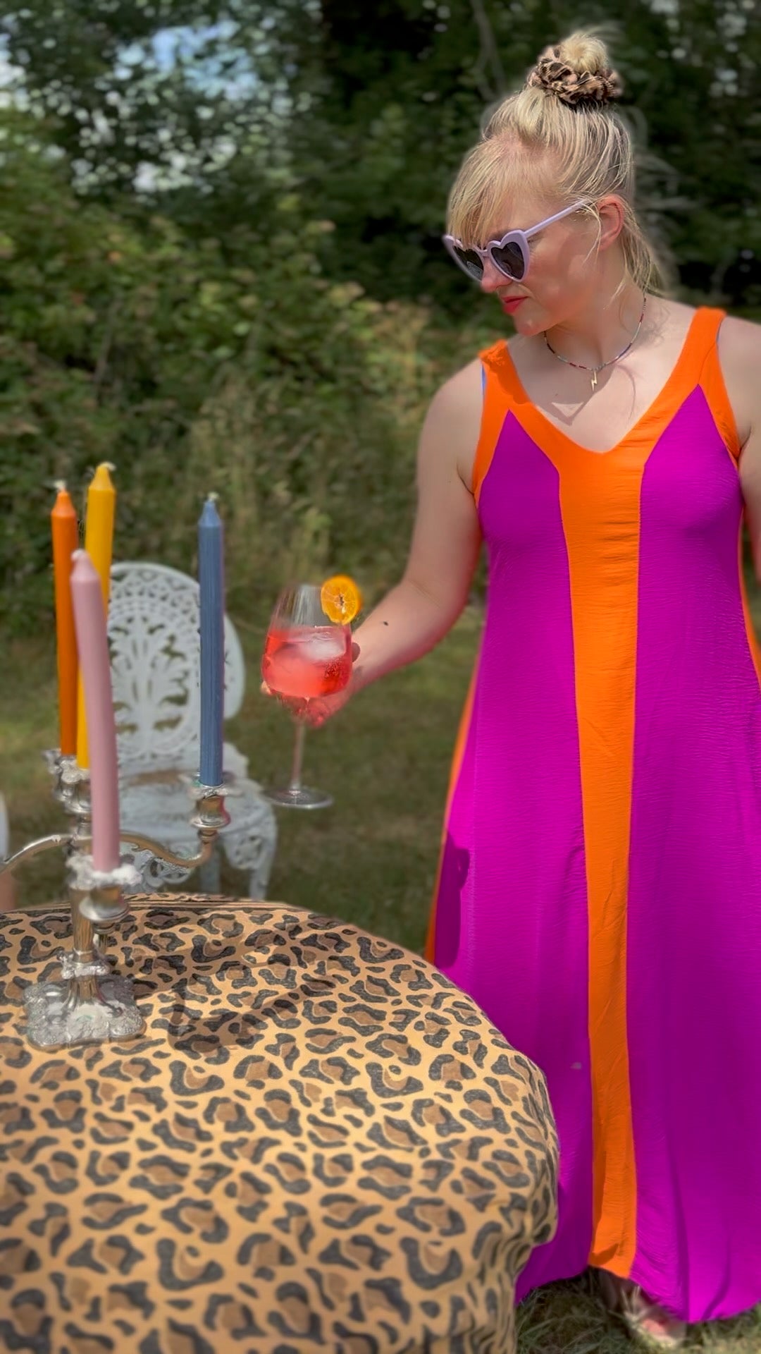 Woman in a colorful dress holding a cocktail near a table with candles outdoors.