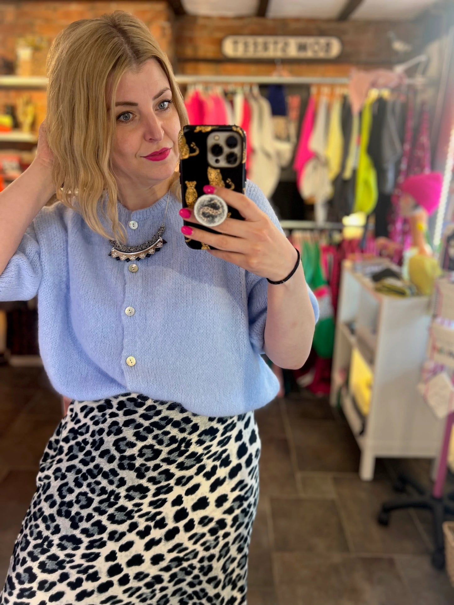 Person taking a mirror selfie wearing a light blue sweater and leopard print skirt in a store.