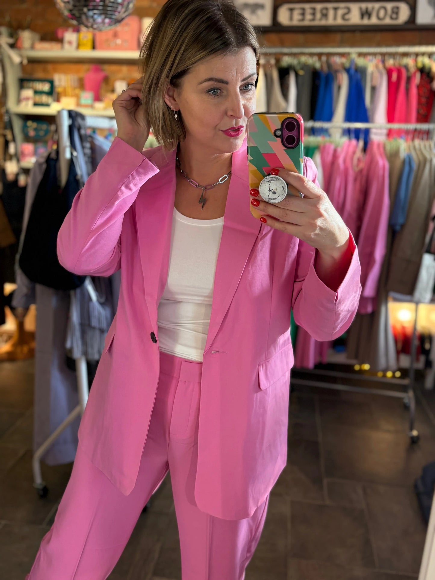 Woman in a pink suit taking a mirror selfie in a clothing store.