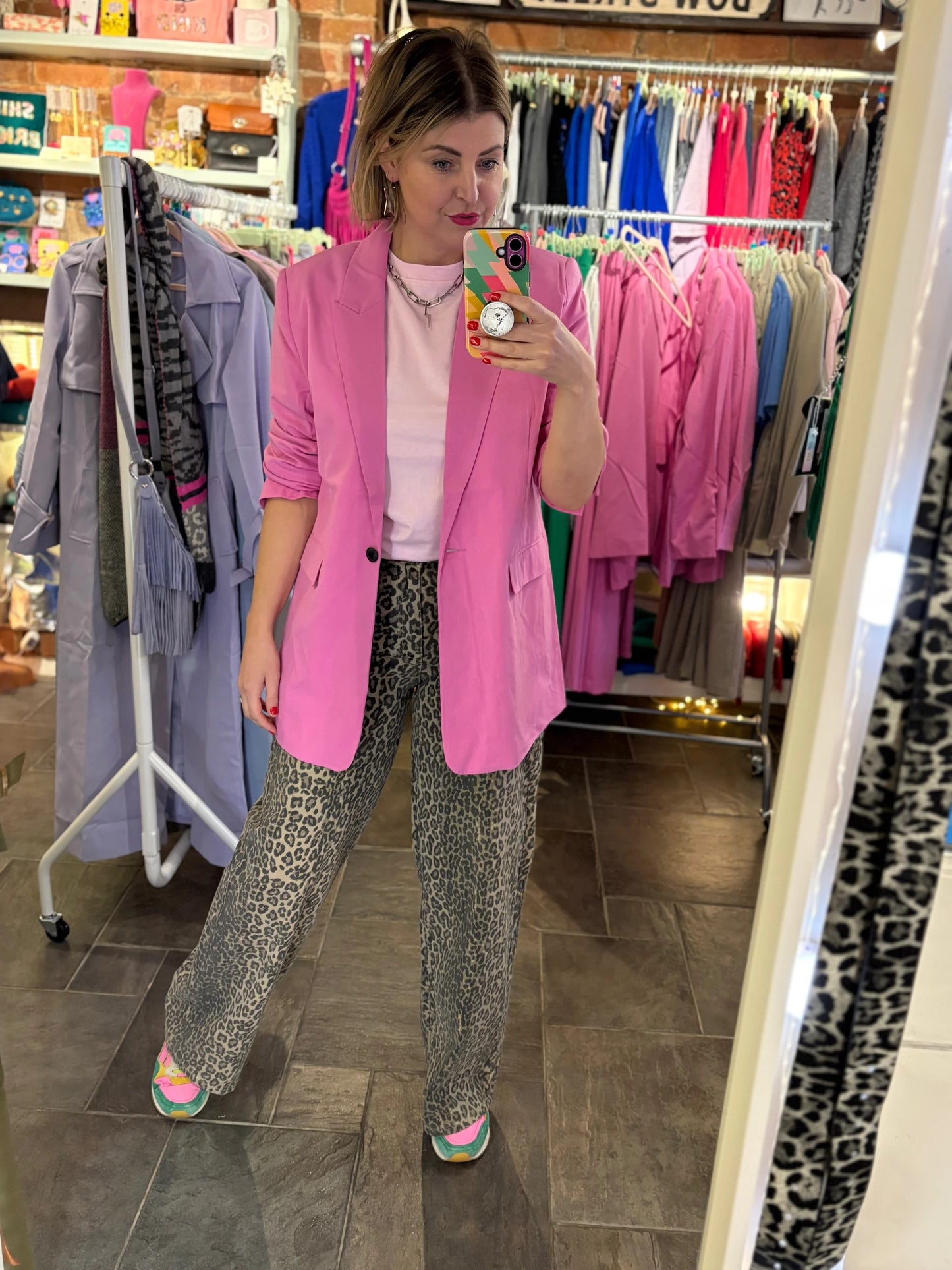 Woman taking a mirror selfie wearing a pink blazer and patterned pants in a clothing store.