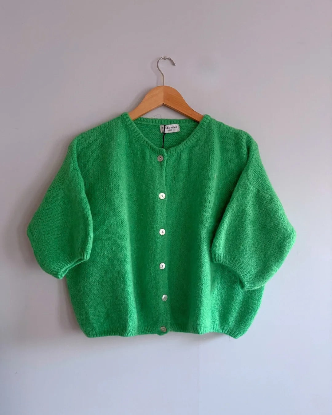 Green cardigan on a wooden hanger against a white background
