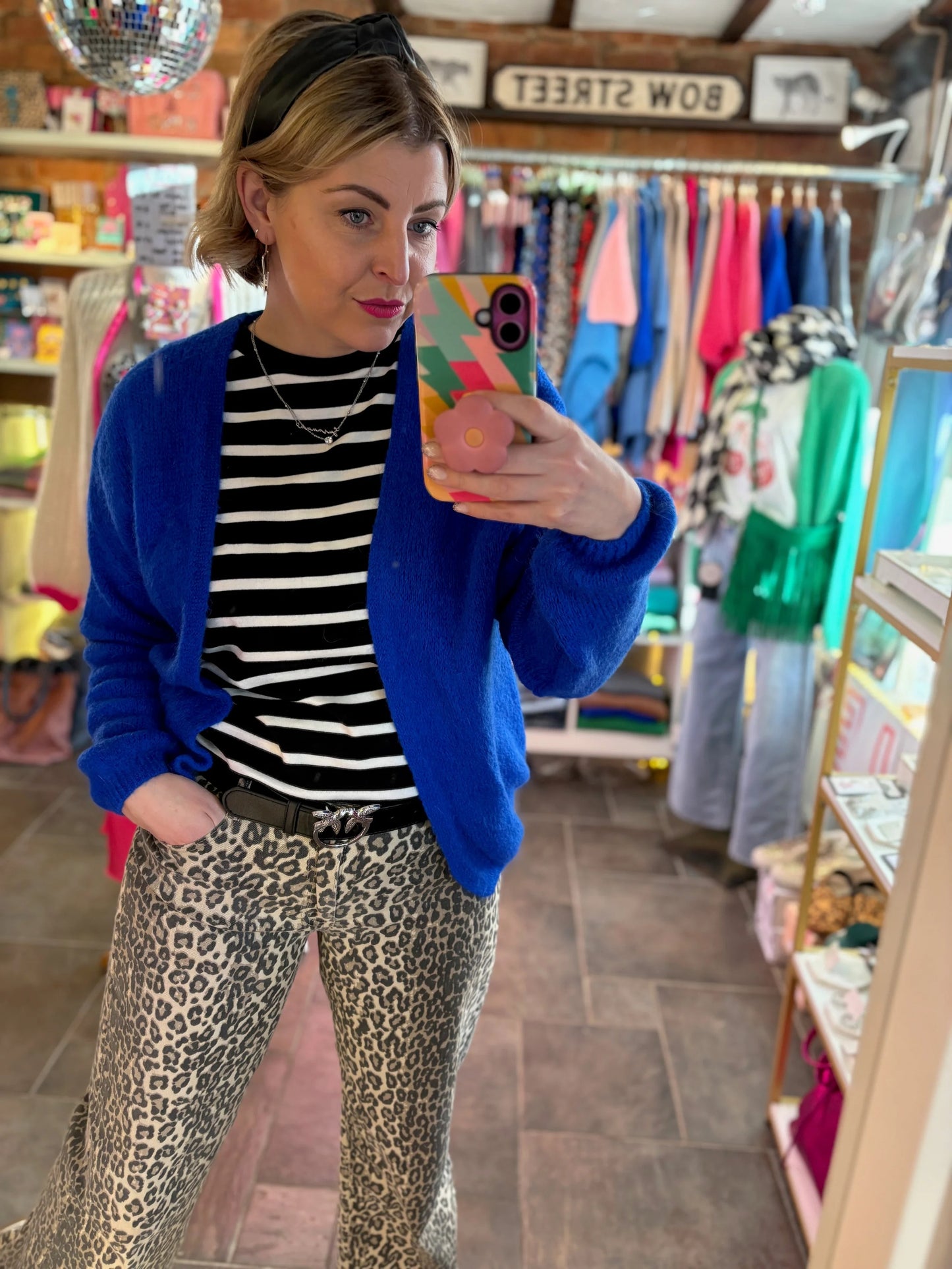 women in shop taking selfie with bright blue cardigan and leopard print jeans