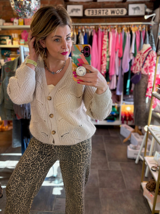 Woman taking a mirror selfie wearing a beige cardigan and leopard print pants in a store.