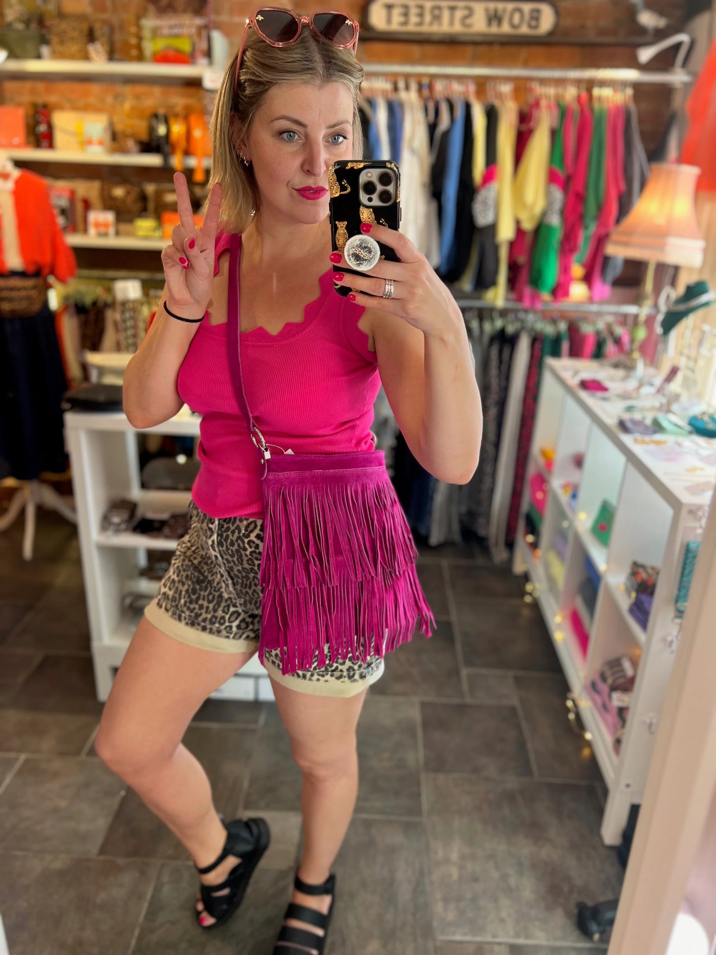 Woman taking a mirror selfie wearing a pink top and fringed skirt in a store.