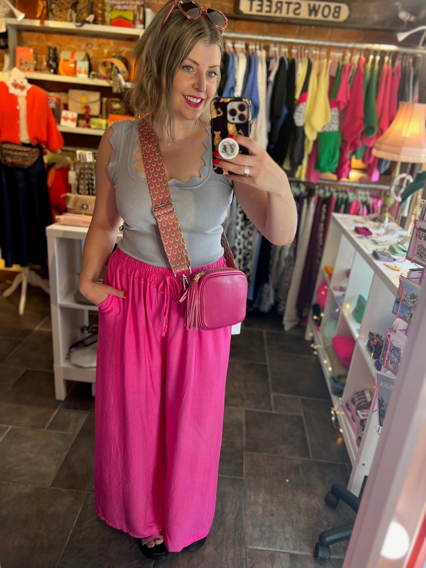 Woman taking a mirror selfie in a clothing store wearing a pink dress and carrying a pink bag.