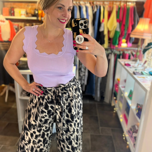 Woman taking a mirror selfie wearing a light purple top and leopard print pants in a store.