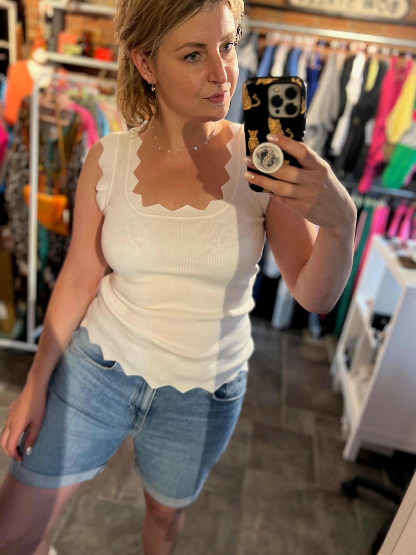 Woman taking a mirror selfie wearing a white top and denim shorts in a clothing store.