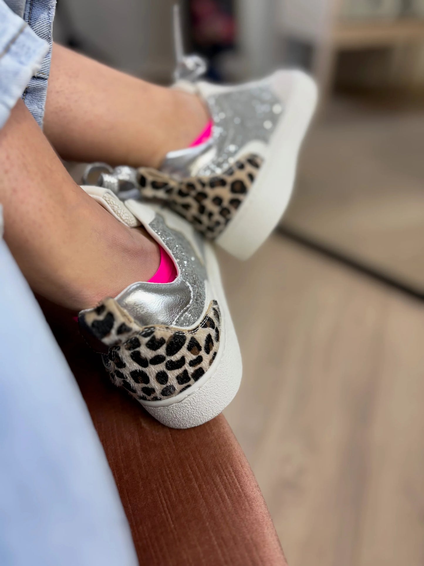Close-up of leopard print sneakers with glittery accents worn by a person.