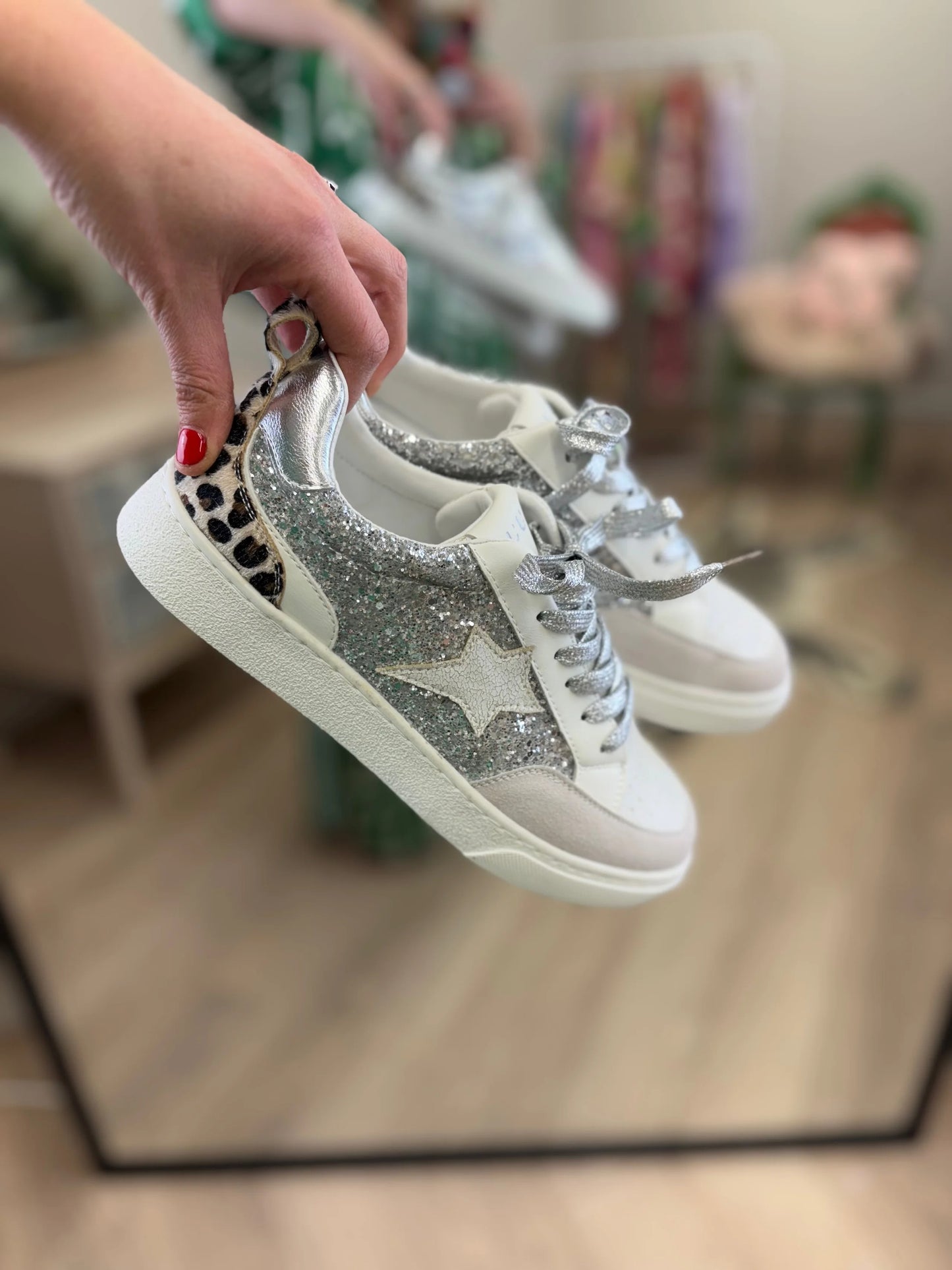 White sneakers with silver star designs held by a hand.
