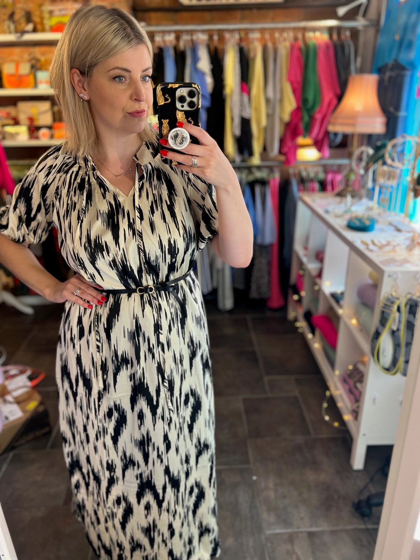 Woman taking a mirror selfie wearing a black and white patterned dress in a clothing store.