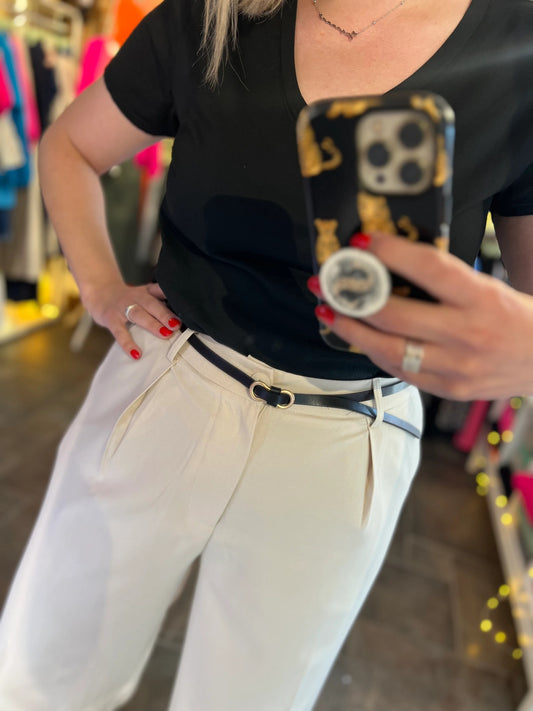 Person taking a mirror selfie wearing a black top and white pants in a store setting.