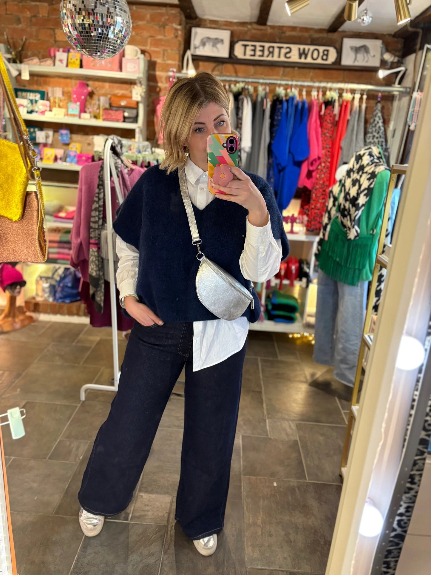 Person taking a mirror selfie in a clothing store with various garments on racks.