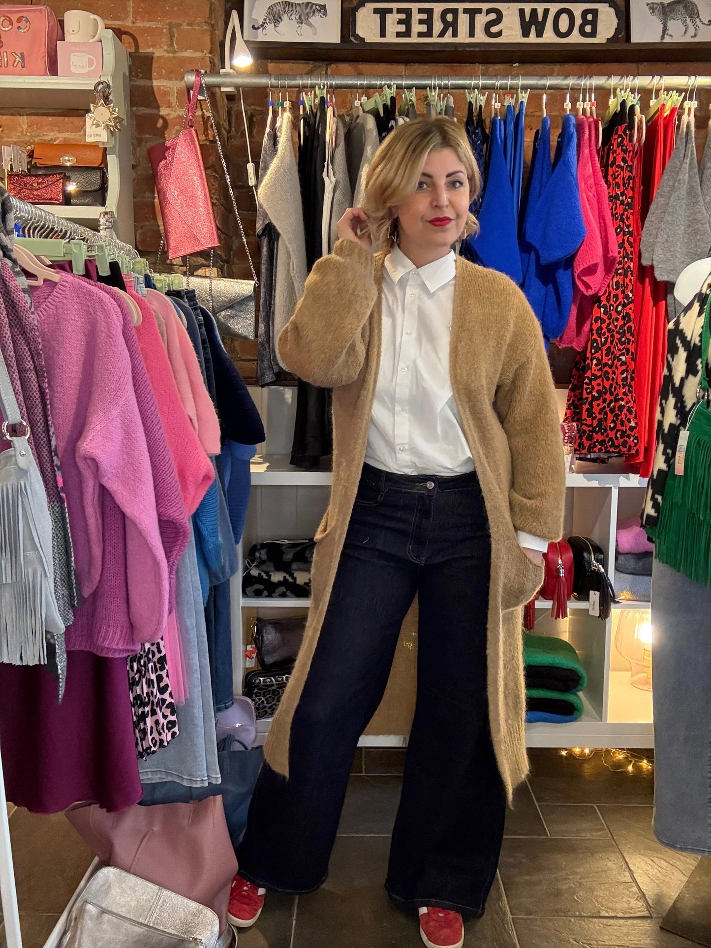 Woman in a clothing store wearing a beige cardigan and white shirt.