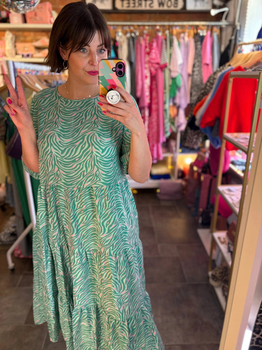 Woman in a green dress taking a mirror selfie in a clothing store.