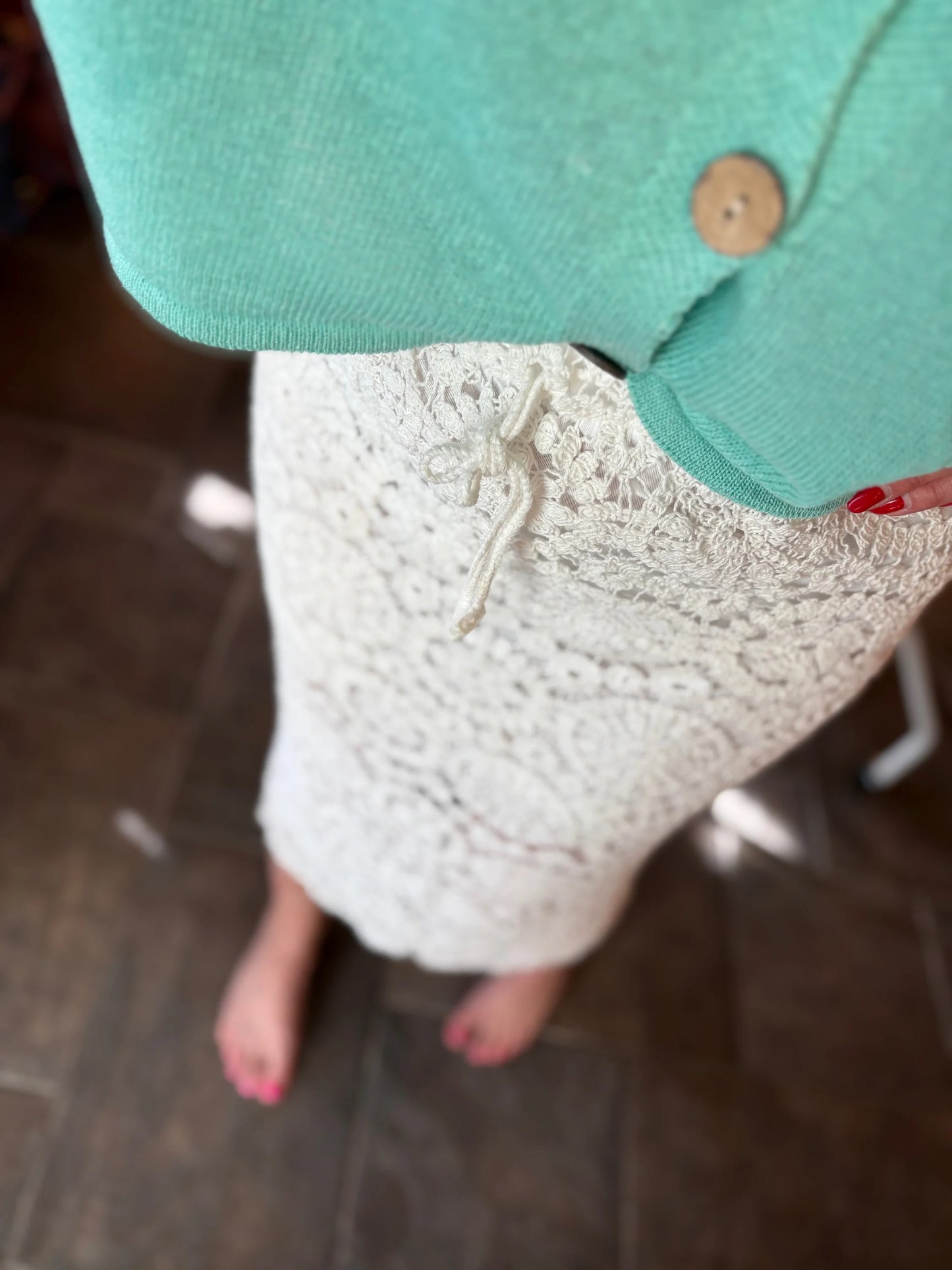 Close-up of a person wearing a green cardigan over a white lace top.