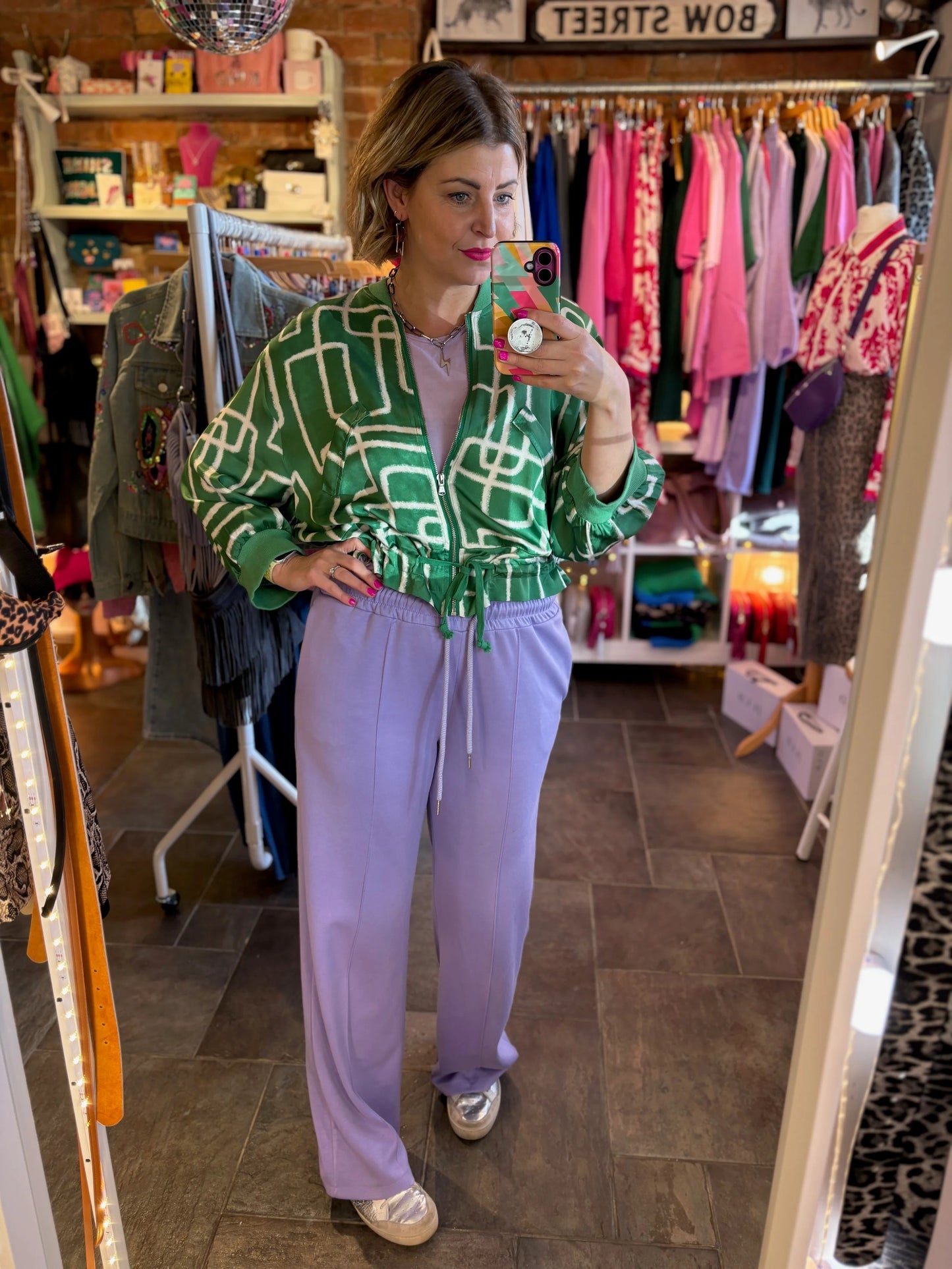 Person wearing a green patterned jacket and purple pants in a clothing store.