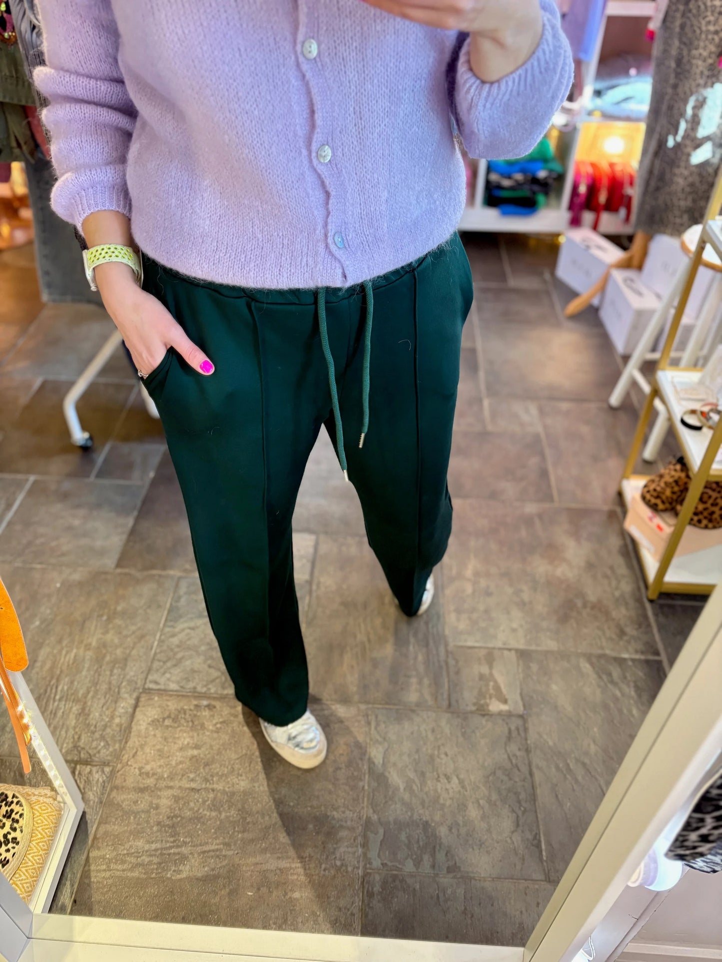 Person wearing a light purple sweater and dark green pants in a store setting.
