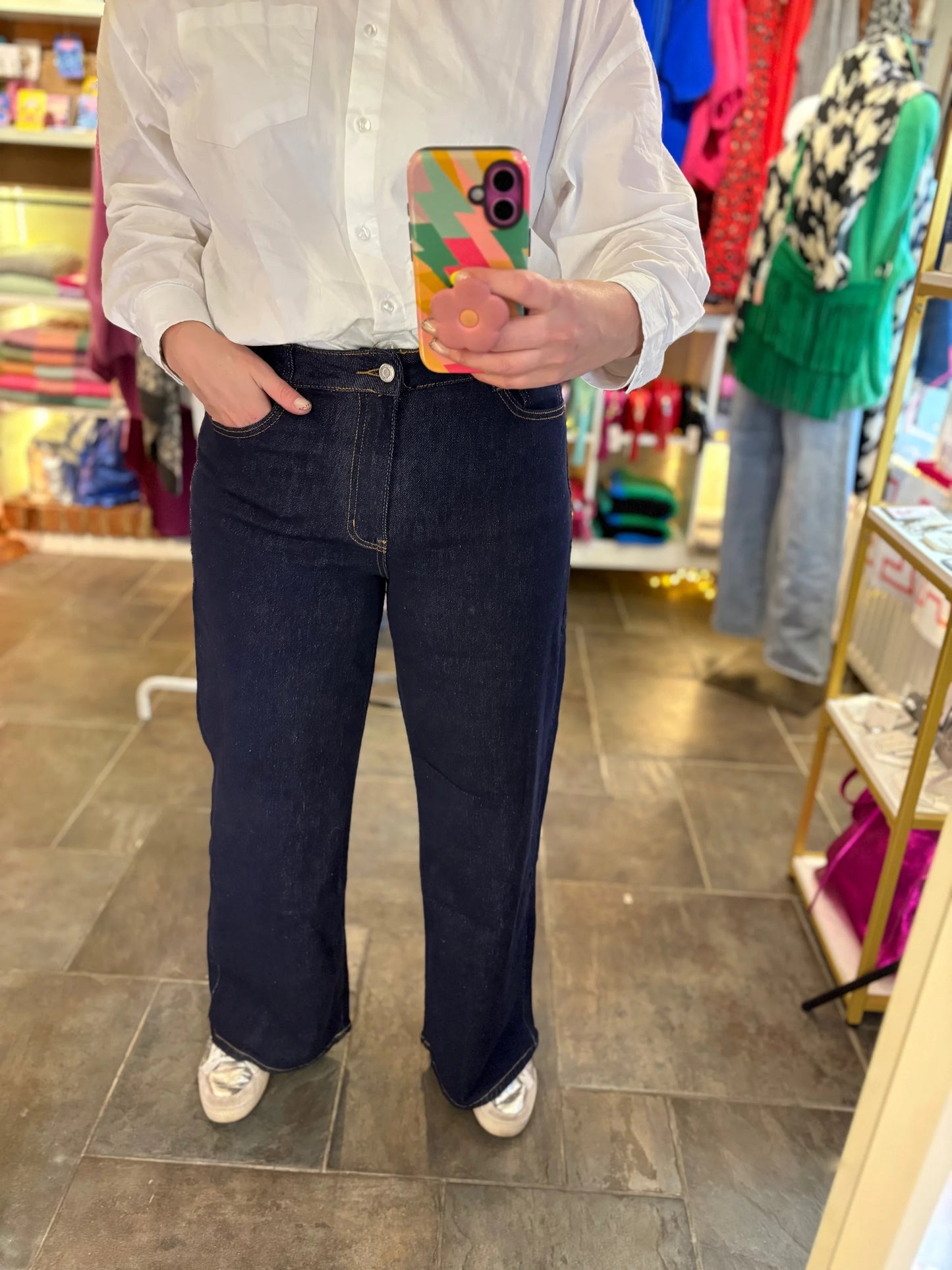 Person wearing a white shirt and dark jeans holding a colorful phone case in a store setting.