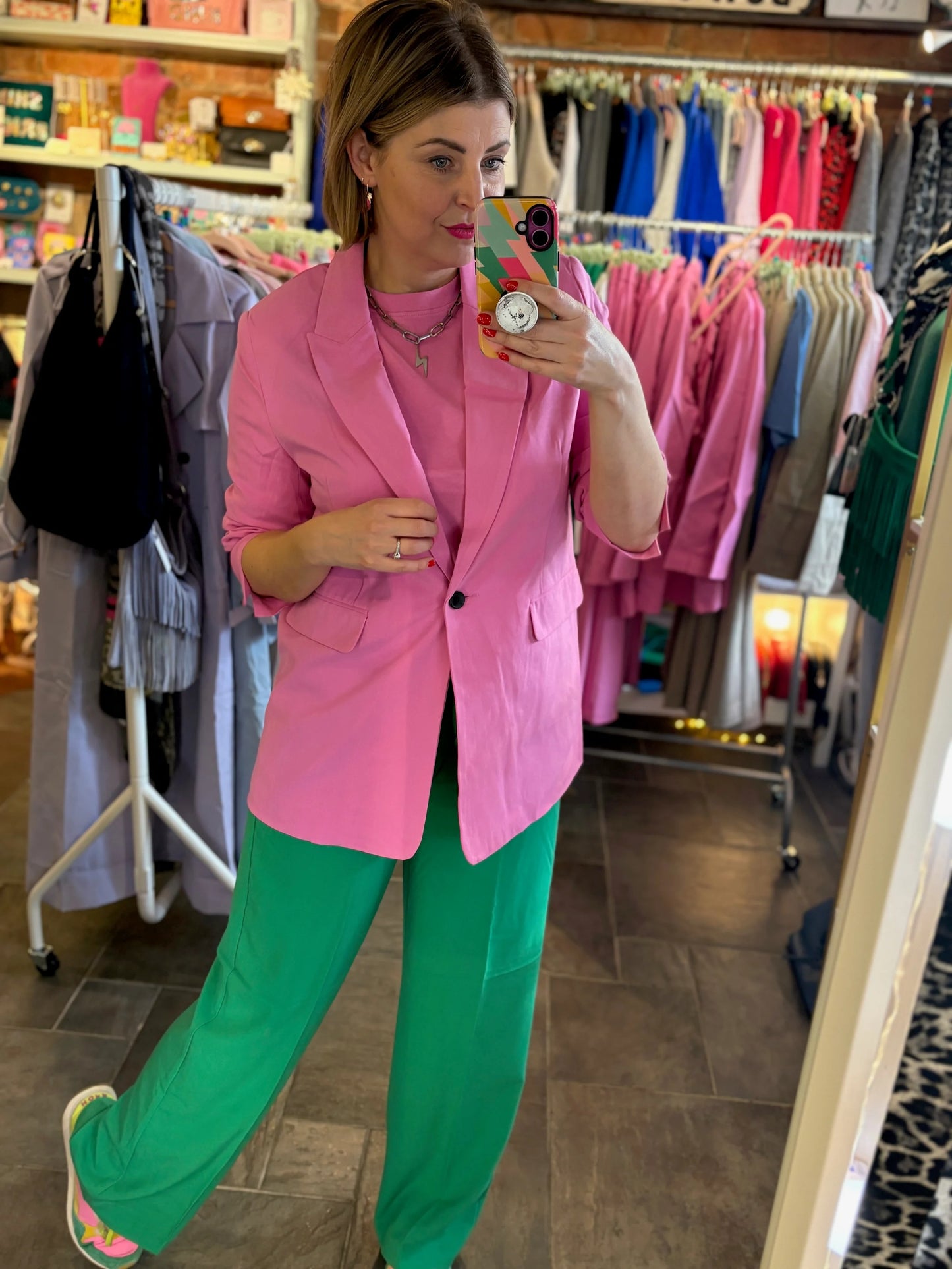 Person wearing a pink blazer and green pants in a clothing store.