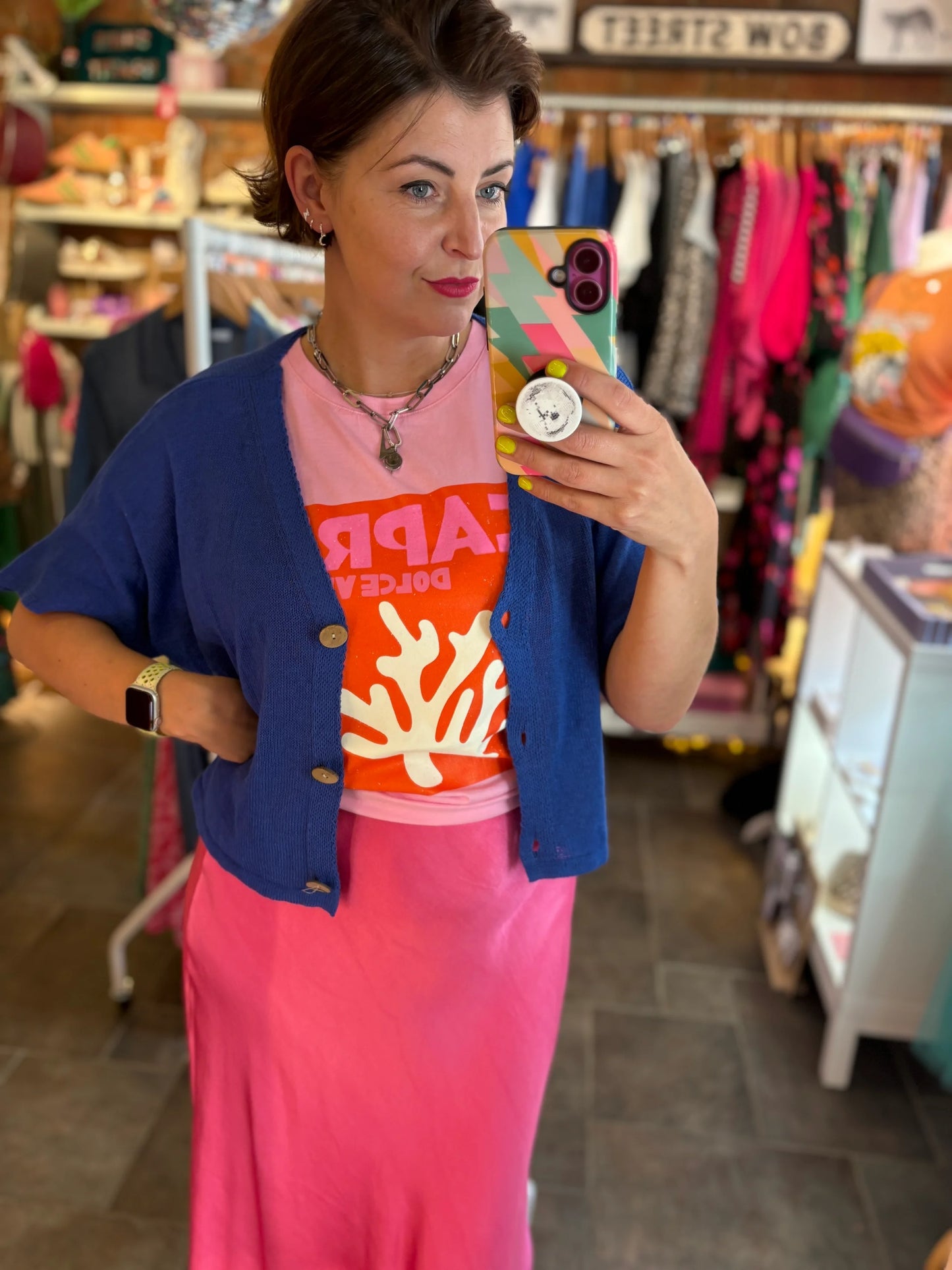 Woman taking a mirror selfie in a store wearing a colorful outfit.