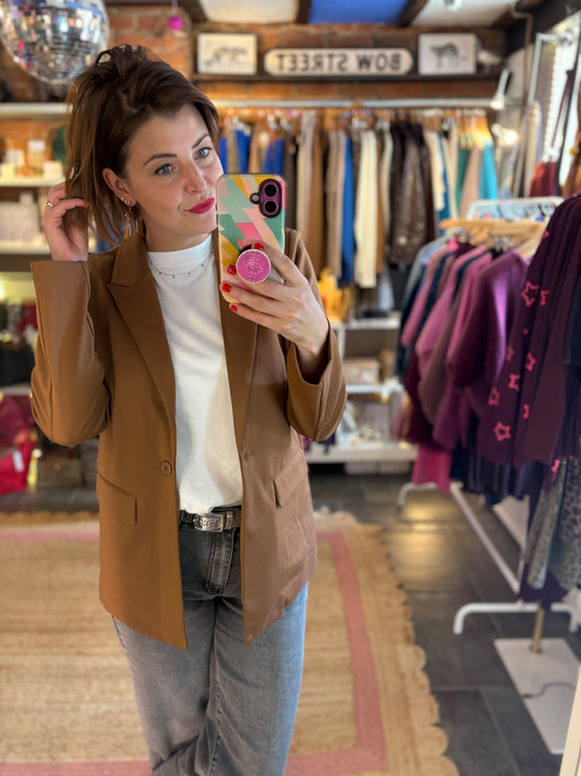 Woman taking a mirror selfie wearing a brown blazer, white t-shirt and jeans in a clothing store.
