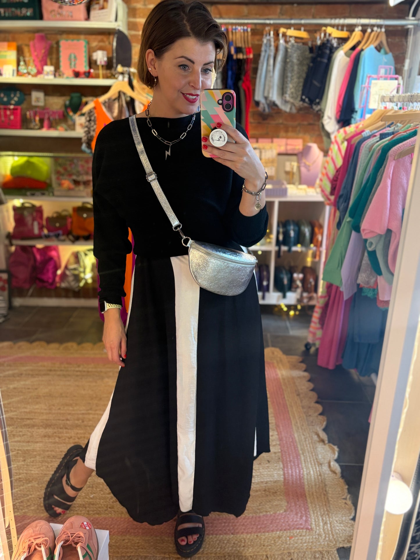 Woman taking a mirror selfie in a clothing store wearing a black dress with white stripes.