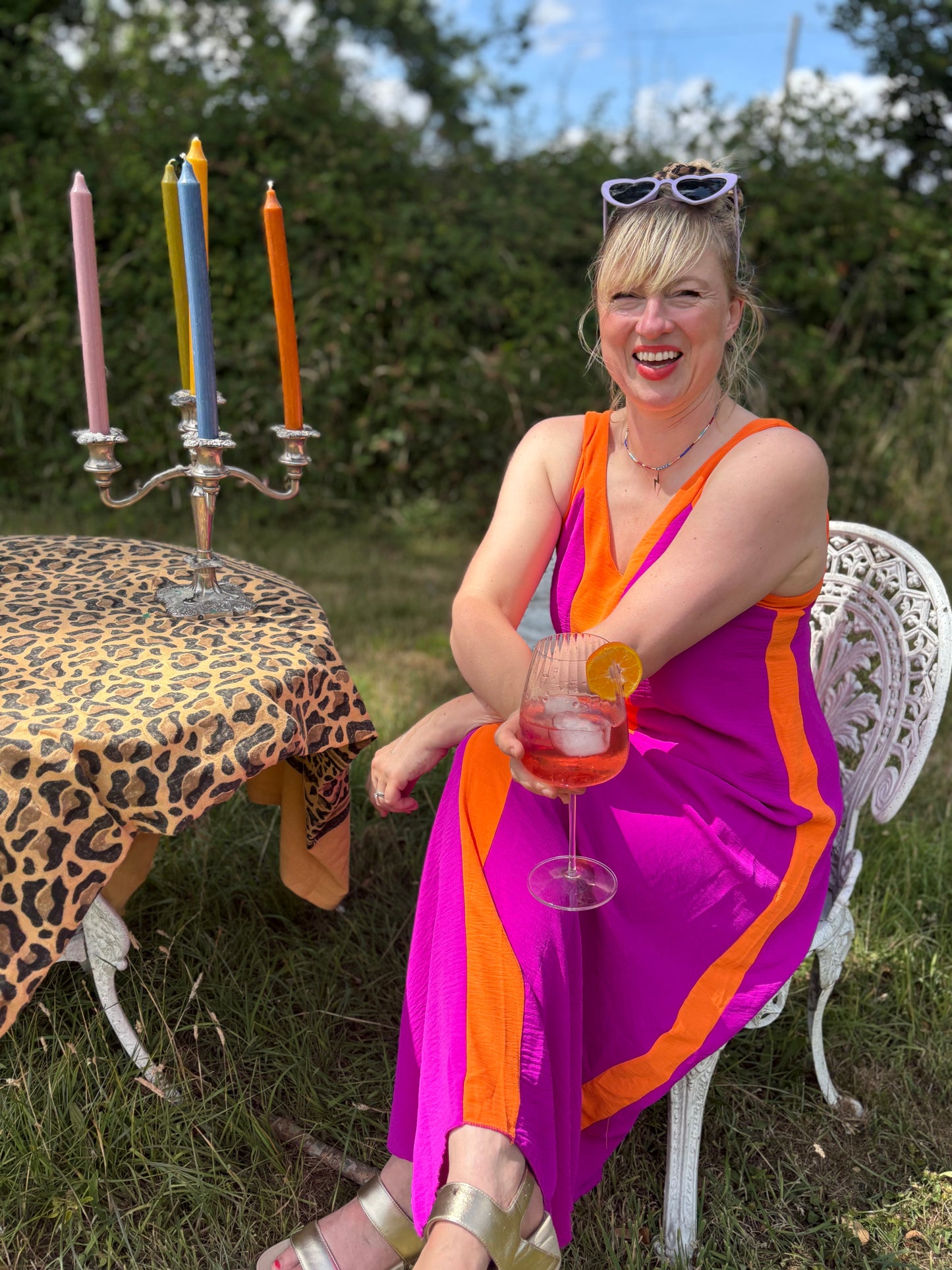 Woman in a colorful dress sitting outdoors with a drink, surrounded by candles and a leopard print tablecloth.