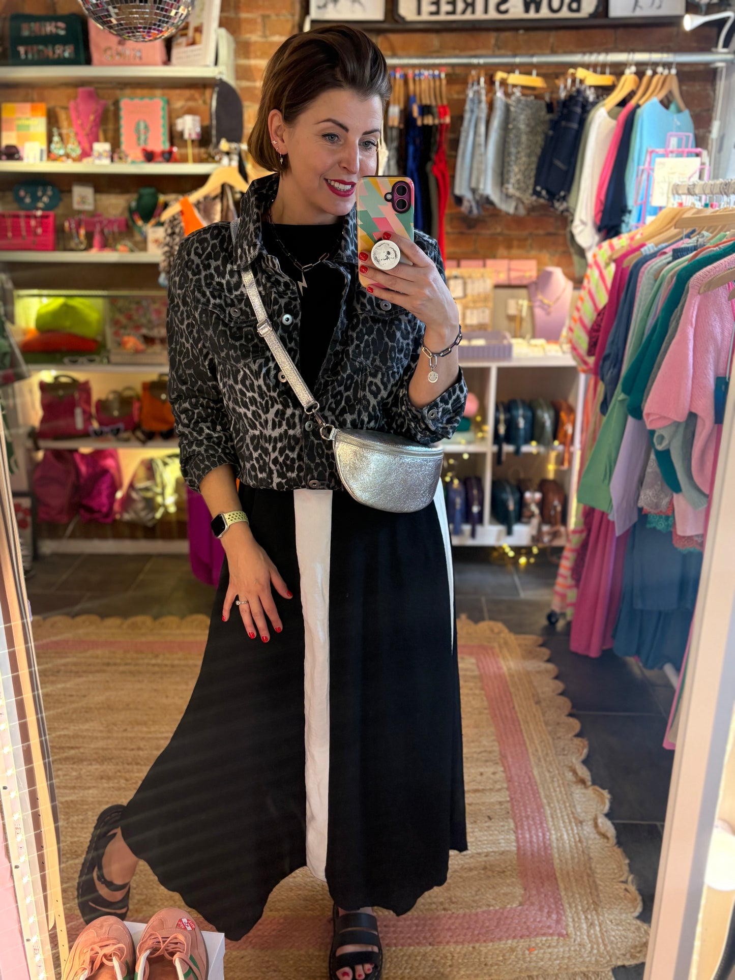Woman taking a mirror selfie in a clothing store with leopard print jacket layered over a black and white dress