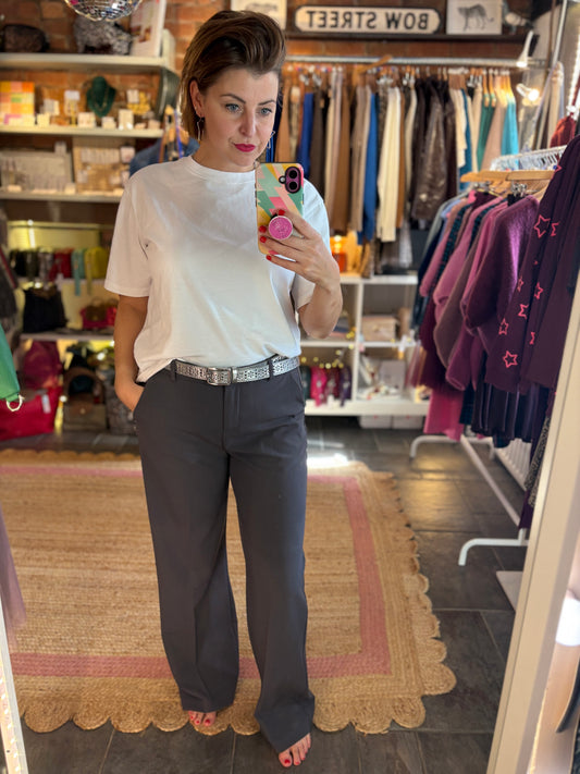 Woman taking a mirror selfie in a clothing store wearing a white top and grey trousers