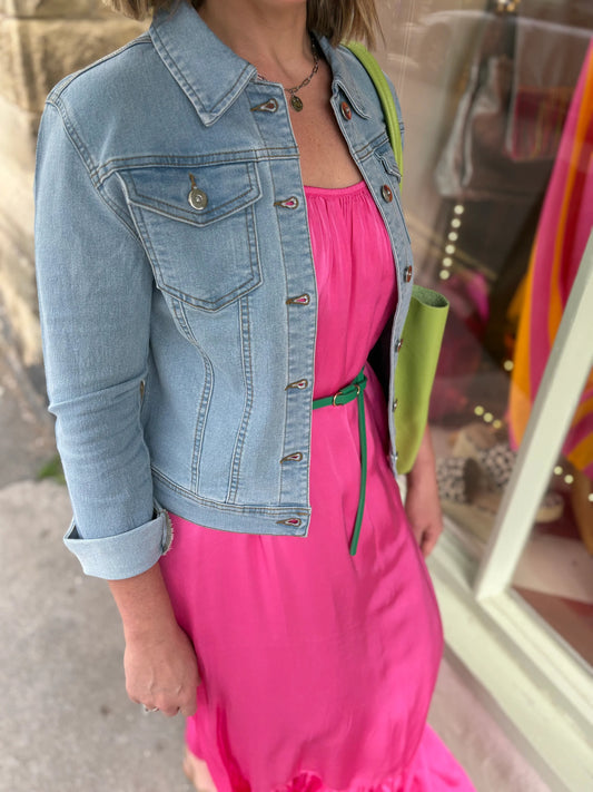 Person wearing a pink dress with a denim jacket and green bag.