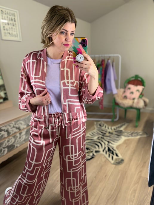 Woman taking a mirror selfie wearing a pink satin patterned co ord set.