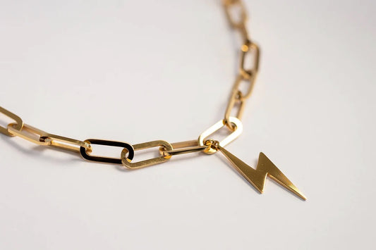 Gold chain necklace with a lightning bolt pendant on a light gray background