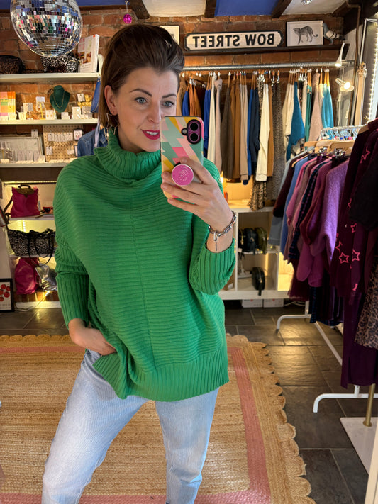 Woman in a green ribbed sweater taking a selfie in a store with light blue jeans