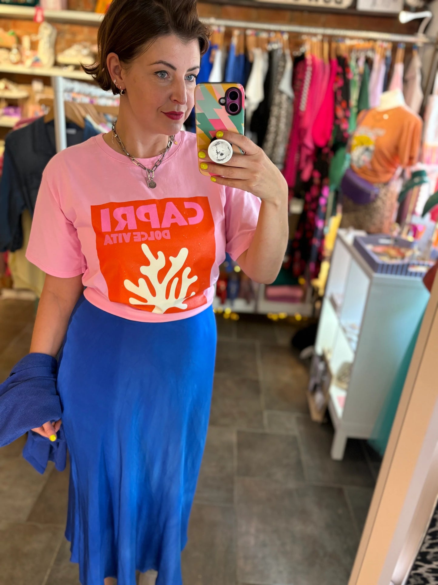 Woman taking a mirror selfie wearing a pink Capri shirt with a coral design in a store.