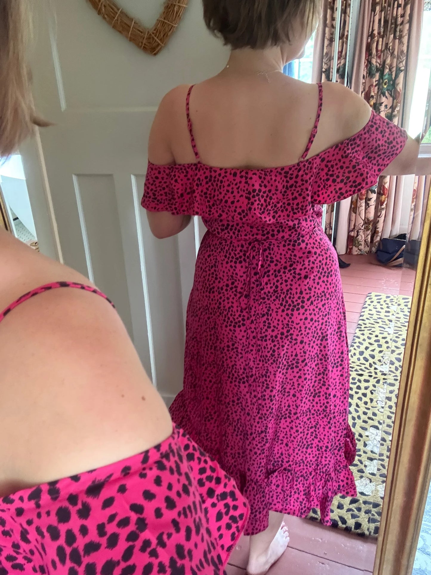 Two women wearing pink dresses with black leopard print patterns indoors.