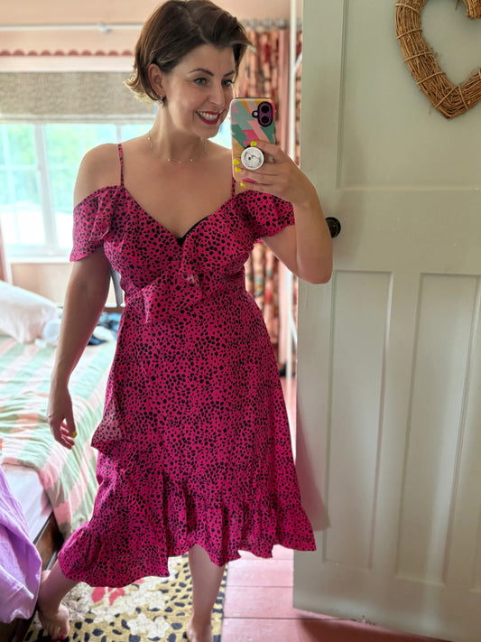 Woman taking a mirror selfie wearing a pink dress with black patterns in a room.