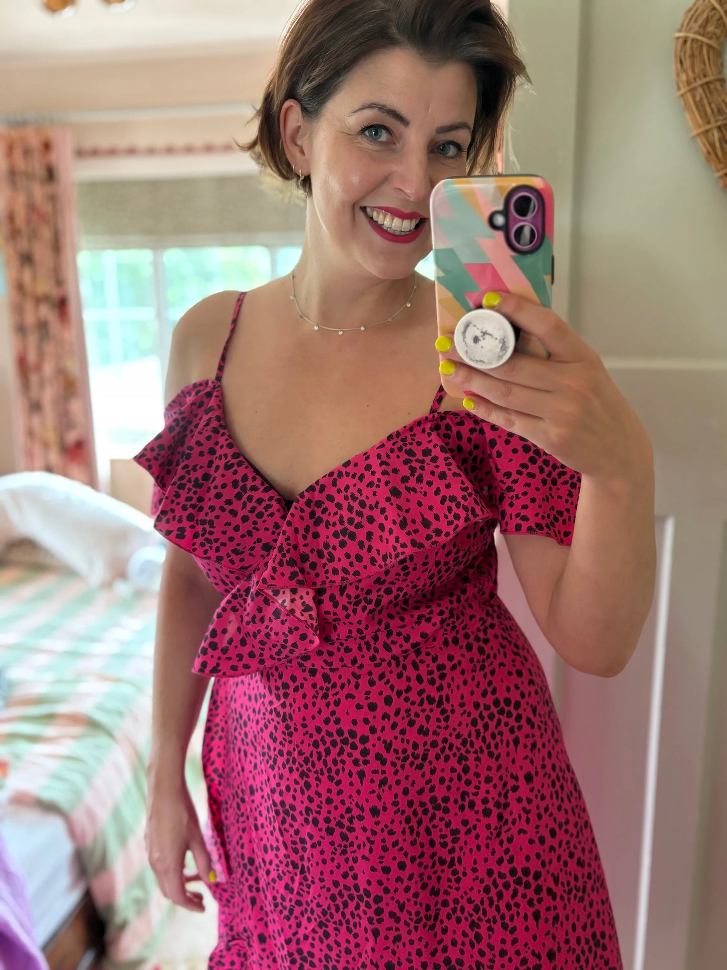Woman in a pink dress taking a mirror selfie with a colorful phone case.