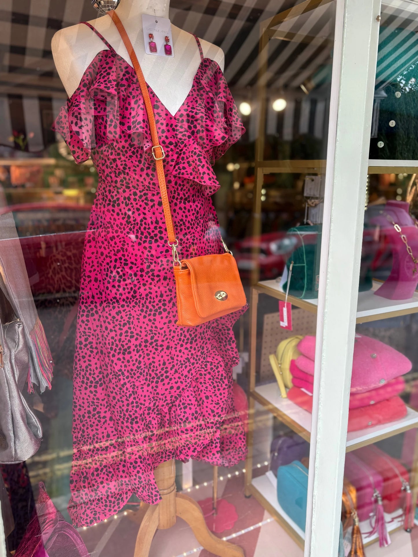 Mannequin wearing a pink dress with a leopard print pattern and an orange handbag inside a store.