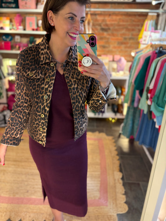 Woman taking a mirror selfie wearing a leopard print jacket and purple skirt in a store.