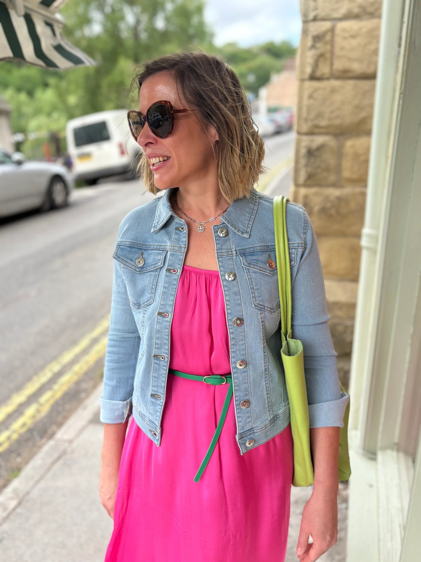 Woman wearing a pink dress, denim jacket, and sunglasses on a street.