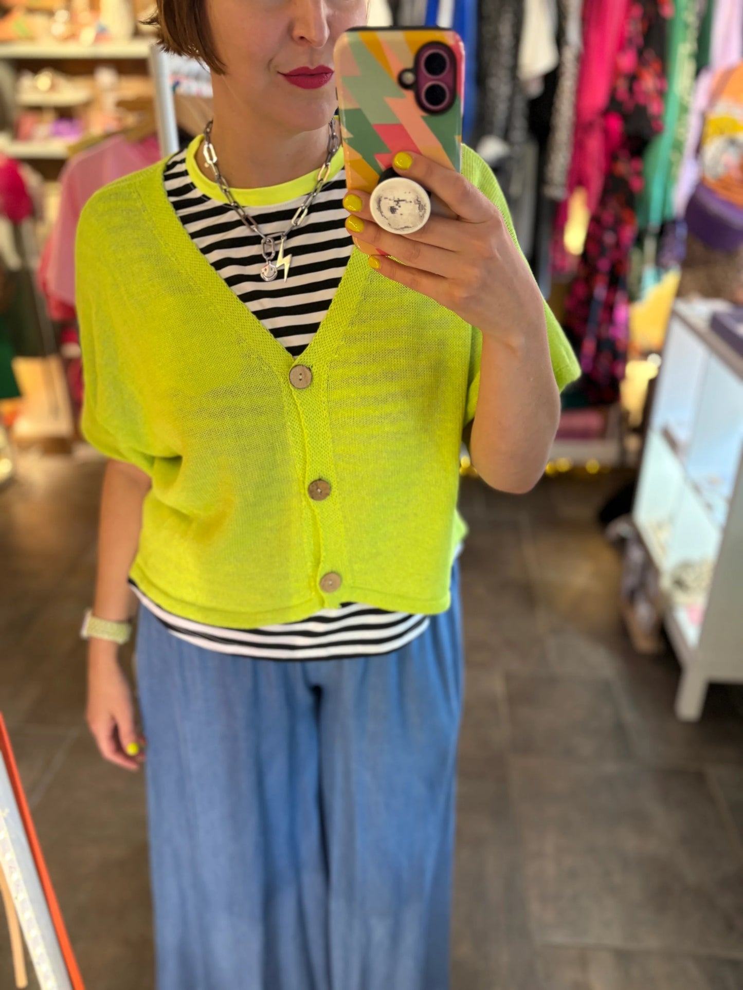 Person wearing a bright yellow cardigan over a striped shirt and blue pants, taking a mirror selfie.